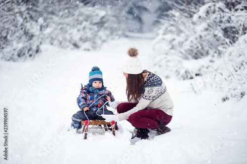 Mother and son having fun in wintertime, enjoy snow, sledge slides on slope