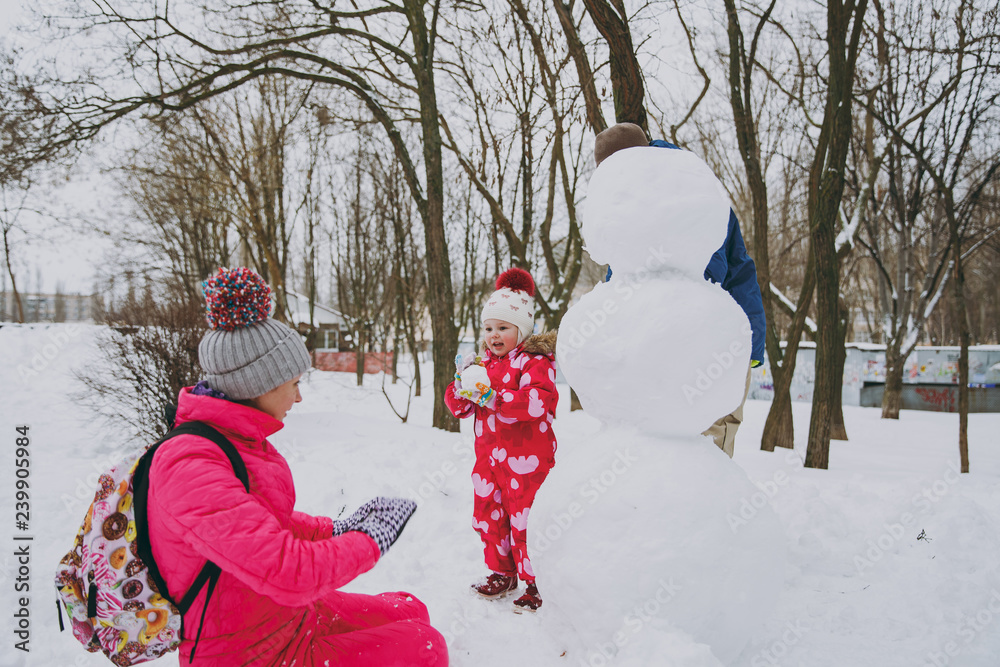 Young family man, woman little girl in warm clothes play making snowballs, snowman in snowy park or forest outdoors. Winter fun, leisure on holidays. Love relationship family people lifestyle concept.