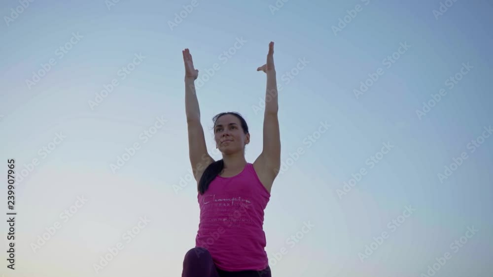 A young woman practices yoga on a mountain in the background of a big city. Healthy woman doing sports at sunset. A female athlete in a pink shirt and purple leggings does a warm-up at sunrise. A young woman practices yoga on a mountain in the background of a big city. Healthy woman doing sports at sunset. A female athlete in a pink shirt and purple leggings does a warm-up at sunrise.
