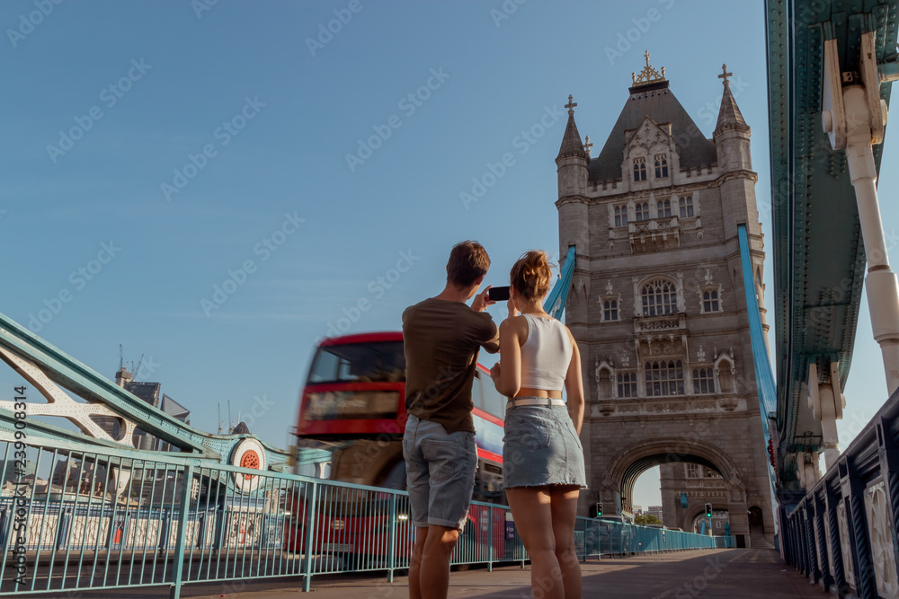 couple is taking a picture of a red double decker bus on the tower bridge in London
