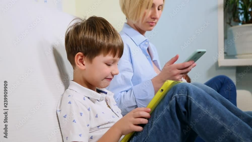 A family of three sit on the couch and uses digital devices. The boy using tablet and mother browsing information on the smartphone while breastfeeding baby A family of three sit on the couch and uses digital devices. The boy using tablet and mother browsing information on the smartphone while breastfeeding baby