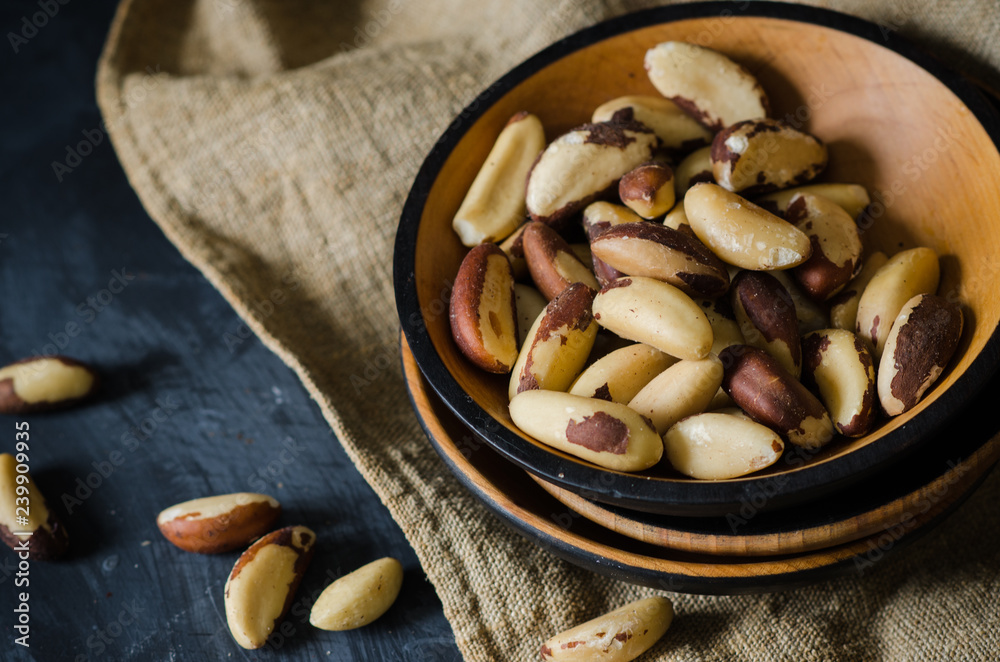 Tasty brasil nuts in a wood plate on linen napkin on black background