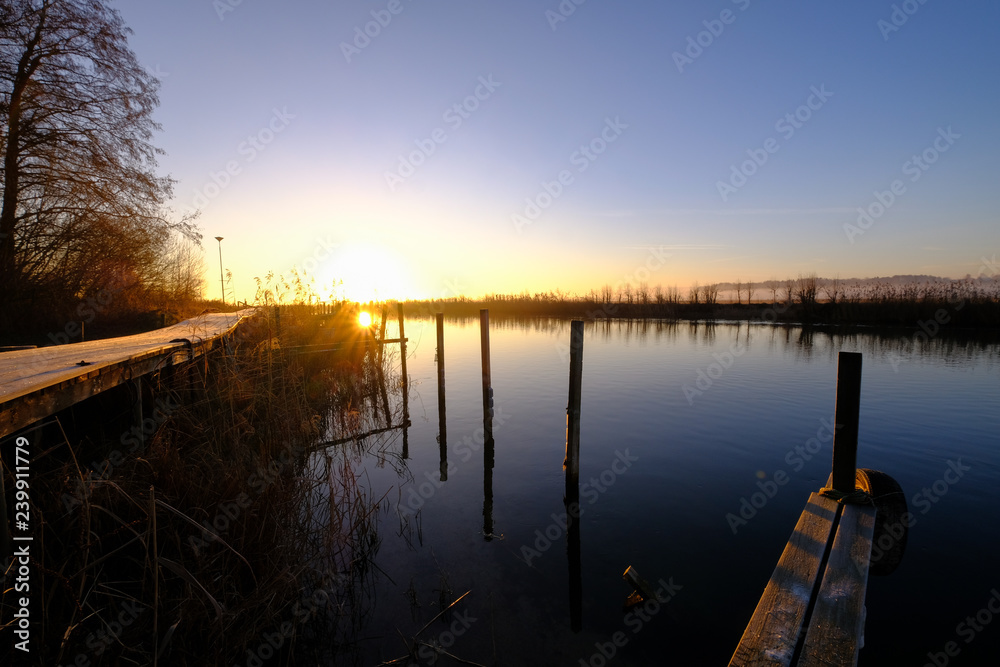 a jetty and wooden piles that stand out of the water surface at sunrise