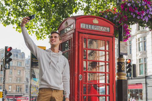 happy young boy taking a selfie in front of a phone box in Londond photo