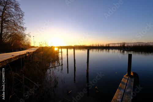 a jetty and wooden piles that stand out of the water surface at sunrise