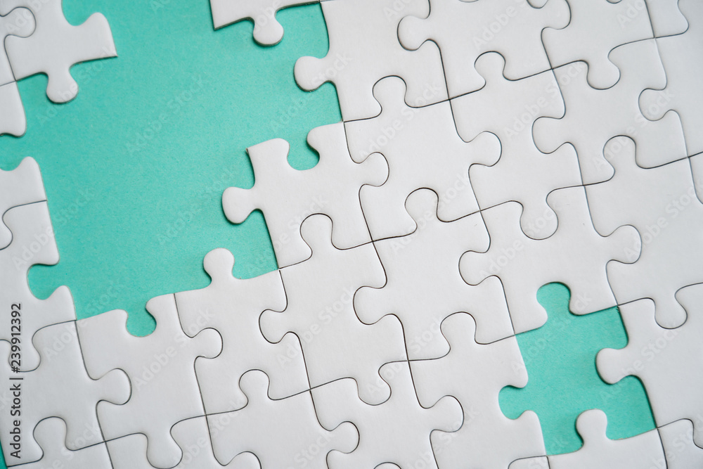 Fragment of a folded white jigsaw puzzle and a pile of uncombed puzzle elements against the background of a colored surface. Fragment of a folded white jigsaw puzzle and a pile of uncombed puzzle elements against the background of a colored surface.