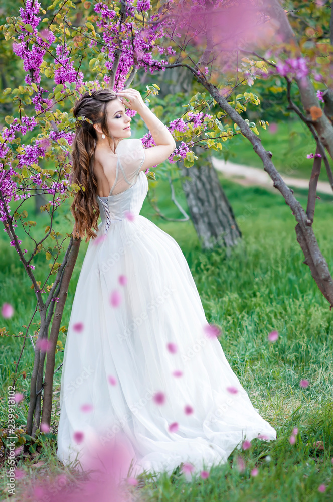 The happiest bride in the world. A beautiful bride poses in her wedding day in a flowered park. Stylish beautiful girl in a wedding dress and lame hair. Wedding make up. Stock Photo