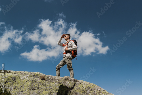 young man with big backpack walking to reach the top of the mountain during a sunny day. contemplating the panorama
