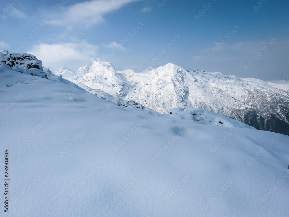 Snowy mountain slope with high peaks in background against a blue sky