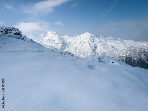 Snowy mountain slope with high peaks in background against a blue sky © CoreyOHara