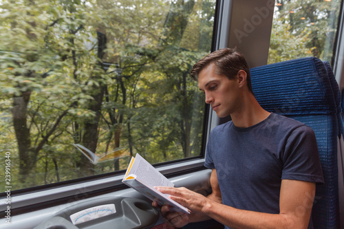 young handsome man reading a book while travelling by train