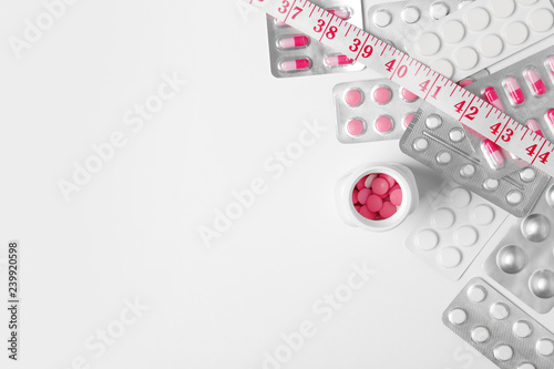 Composition with weight loss pills and measuring tape on white background, top view. Space for text