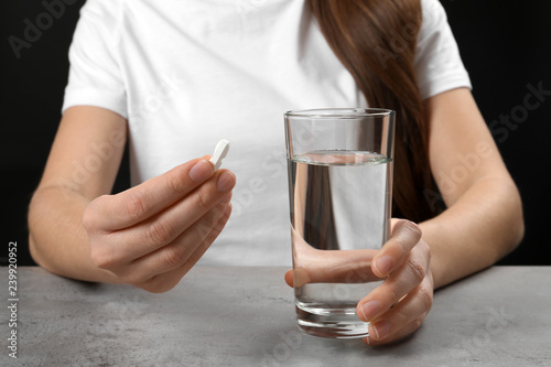 Woman holding pill and glass of water at table, closeup