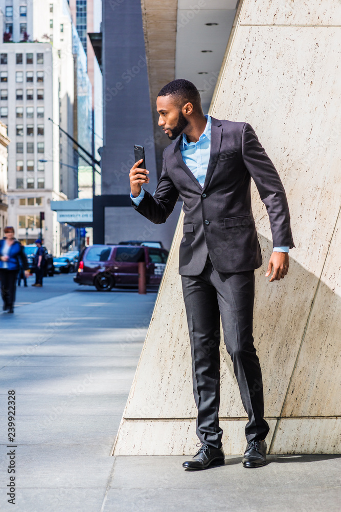 Man waiting for you. Dressing in black blazer, gray pants, brown leather  shoes, African American businessman sitting on railing in vintage style  office, looking at his wristwatch. Time is money.. Stock Photo