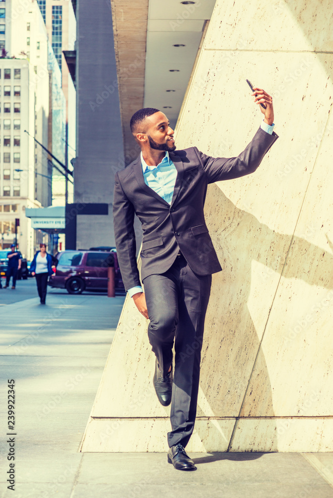 Young African American Businessman with beard, stretching arm, taking selfie on cell phone outside office in New York City, Concept of self assured, self esteem, self checking, confident, success..