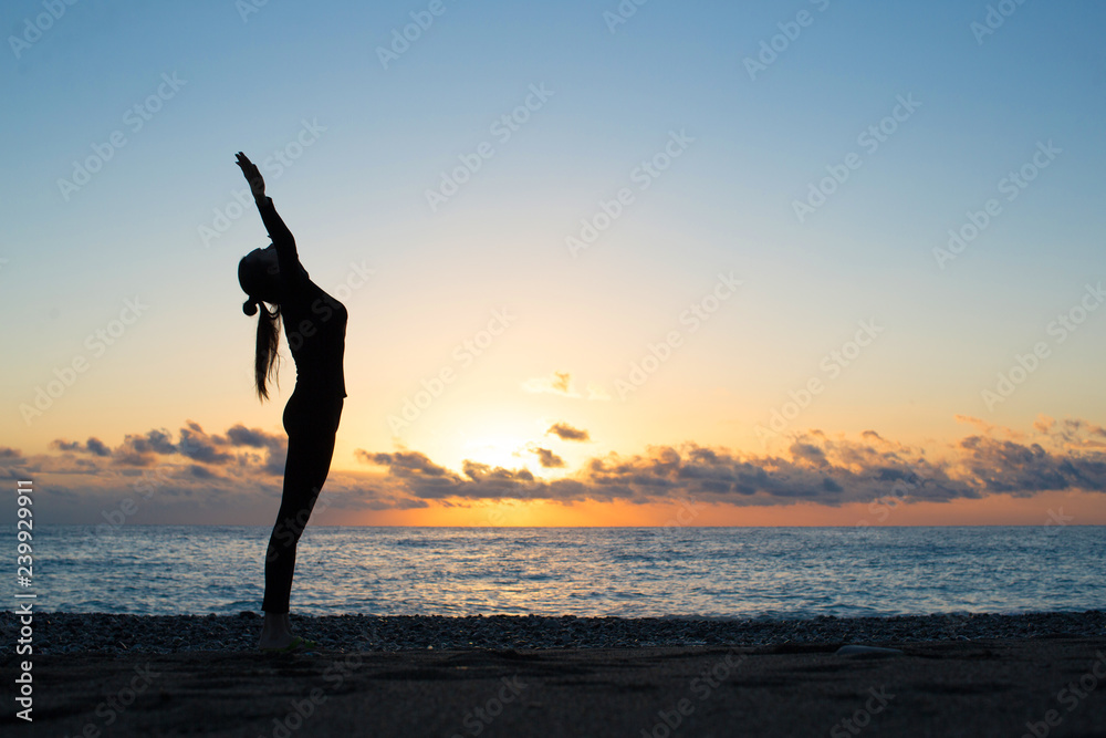 Human silhouette doing yoga on the beach at the dawn