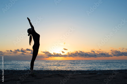 Human silhouette doing yoga on the beach at the dawn
