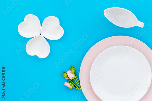 Elegant table setting with white and rose plates and floral decor on blue background top view