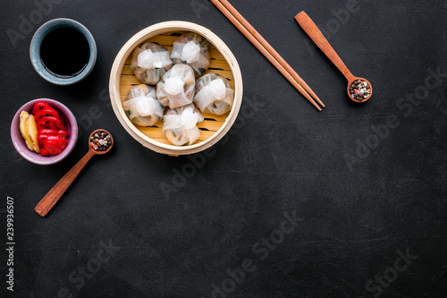 Dim sums with red pepper and vegetables with sticks and black tea in Chinese restaurant on black background top view mockup