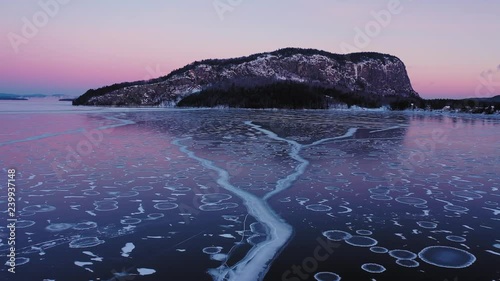 Flying low and slow at dawn over the cracks in a frozen lake towards the cliff face of an isolated mountain photo
