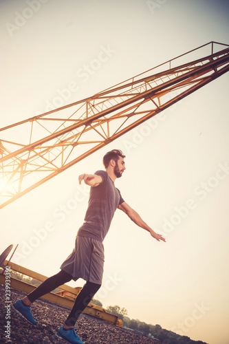 Young man exercising outdoors by the crane at sunset