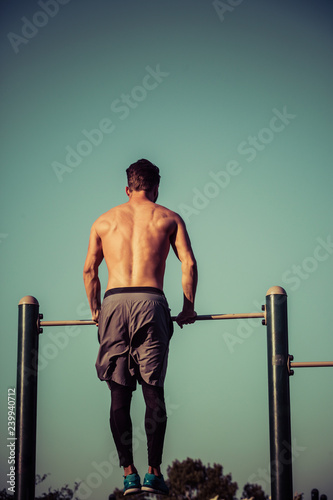 Young man with no shirt on gymnastic bar at park