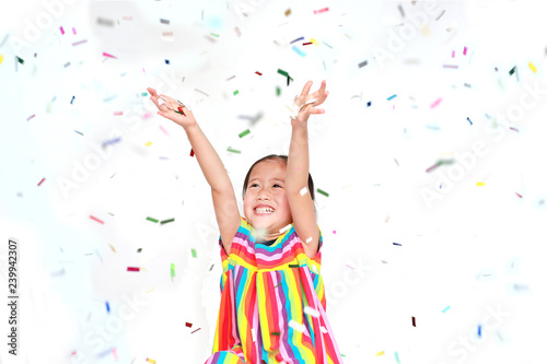 Smiling little Asian kid girl with many falling colorful tiny confetti pieces on white background. Happy New Year or Congratulation Concept.
