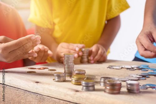 Hands of children are helping putting coins into piggy bank isolated on white background