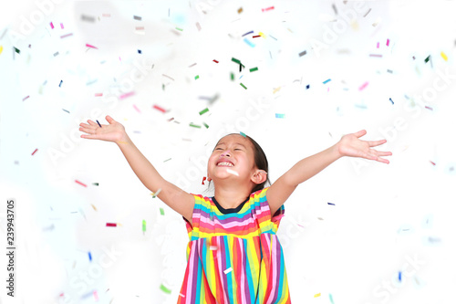Smiling little Asian kid girl with many falling colorful tiny confetti pieces on white background. Happy New Year or Congratulation Concept.
