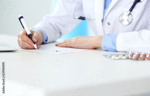 Female doctor filling up prescription form while sitting at the desk in hospital closeup. Healthcare, insurance and excellent service in medicine concept 
