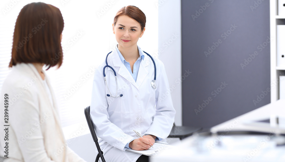 Happy doctor and  patient  discussing something while sitting at the chairs at hospital. Physician at work in clinic. Medicine and healthcare concept
