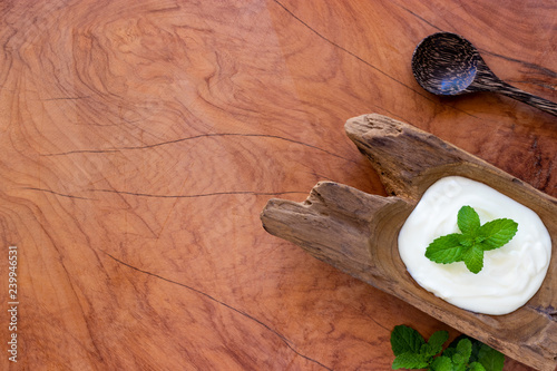 Top view of yogurt in a wooden bowl and mint with spoon on wooden table. Health food concept.