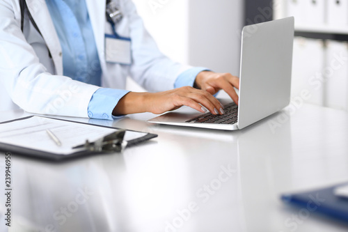 Unknown doctor woman typing on laptop computer while sitting at the desk in hospital office. close-up of hands. Physician at work. Medicine and health care concept © rogerphoto
