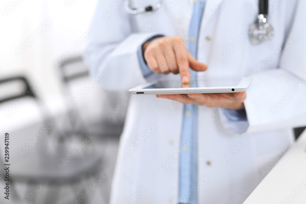 Female physician using digital tablet  while standing near reception desk at clinic or emergency hospital. Unknown doctor woman at work. Medicine concept