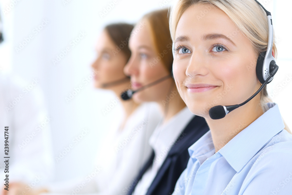 Call center. Group of operators at work. Focus at blonde business woman in headset Call center. Group of operators at work. Focus at blonde business woman in headset