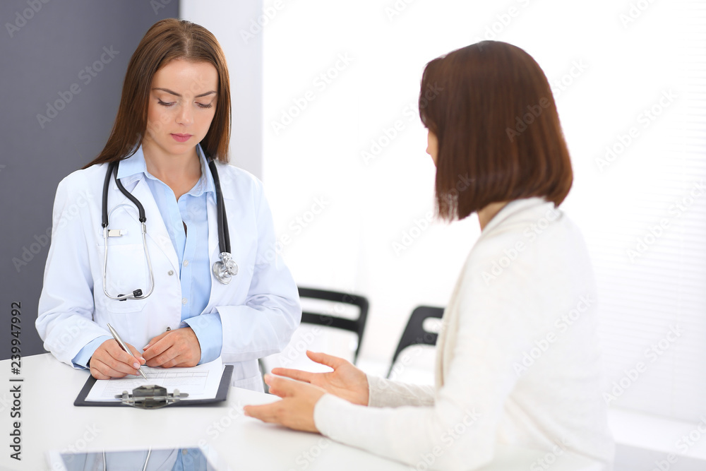 Doctor and patient discussing something while standing near reception desk in emergency hospital. Physician at work in clinic. Medicine and health care concept Doctor and patient discussing something while standing near reception desk in emergency hospital. Physician at work in clinic. Medicine and health care concept