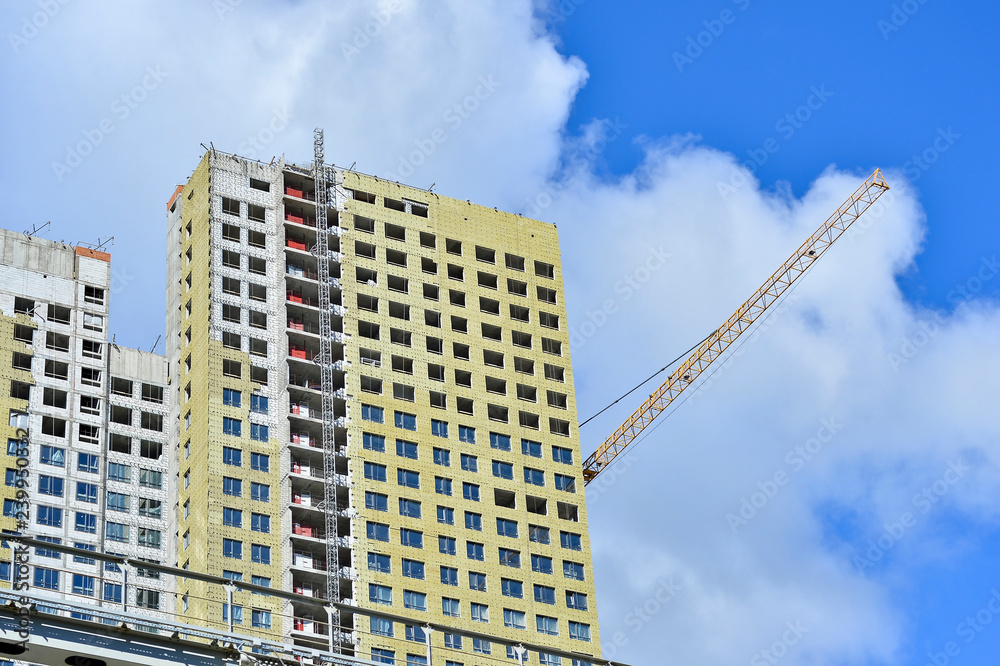 Fototapeta premium Construction of a high-rise building against a blue sky with clouds. Bottom view. In the foreground of the ground branch of the subway