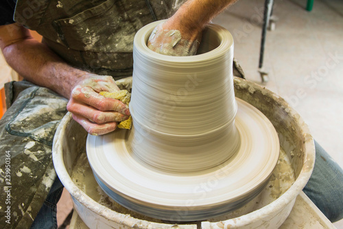  Artist potter in the workshop creating a ceramic vase. Hands closeup. Twisted potter's wheel. Small artistic craftsmen business concept. 