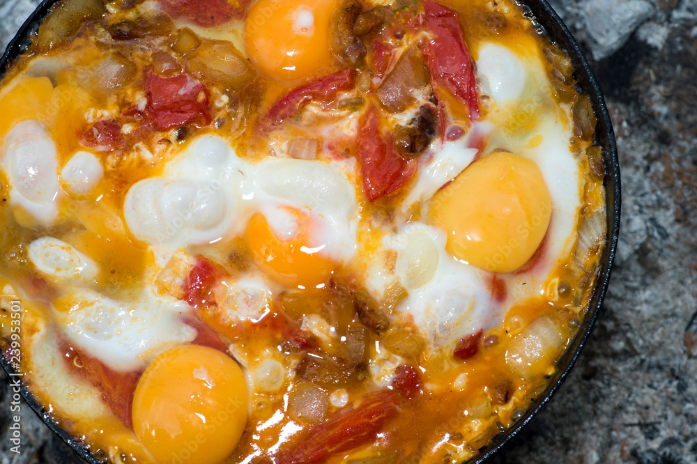 Scrambled eggs with tomatoes is prepared on a black pan on a metal lattice in the journey. The concept of the dish: a combination of protein and fiber Scrambled eggs with tomatoes is prepared on a black pan on a metal lattice in the journey. The concept of the dish: a combination of protein and fiber