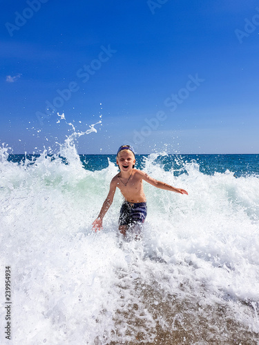 A little blond boy is playing on the seashore  laughing  running away from the waves against the background of huge waves and splashes  Calabria  Italy