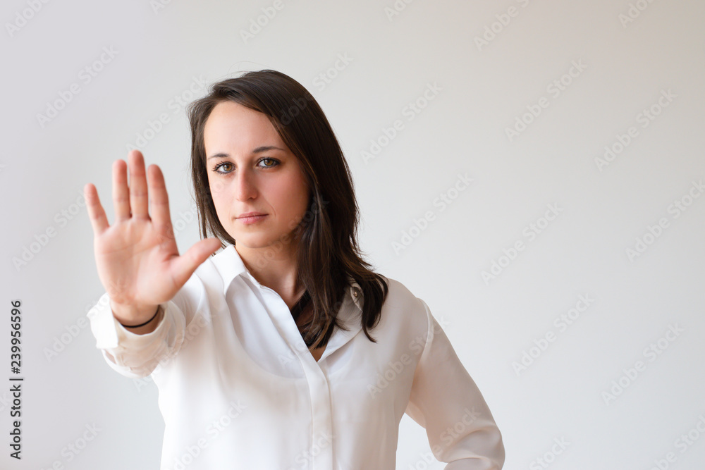 Serious girl in whit shirt showing hand in warning sign. Strict young woman gesturing stop. Warning concept Serious girl in whit shirt showing hand in warning sign. Strict young woman gesturing stop. Warning concept