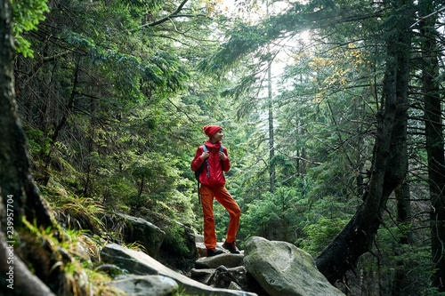 woman hiker with backpack, wearing in red jacket and orange pants, walking in the forest in mountains, Western Ukraine.