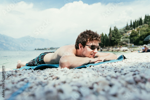 Young handsome man is lying on the beach, sun glasses