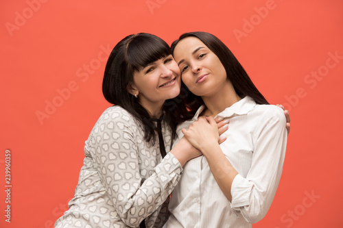 A portrait of a happy mother and daughter at studio on living coral background. Trendy colors. Human positive emotions and facial expressions concept