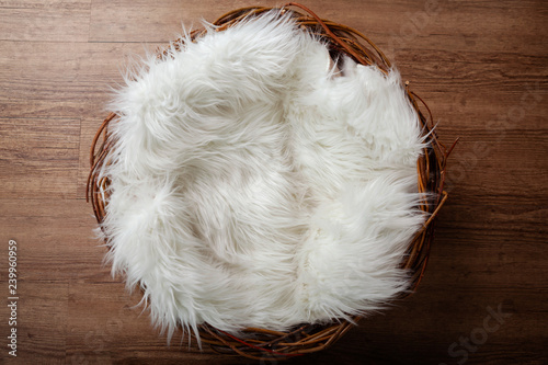 Wooden nest with white flufy sheepskin against an oak wooden floor