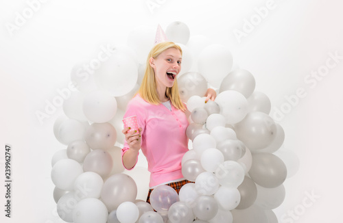 Happy woman in party cap with white air balloons and cup of fruit juice. Joyful model having fun. Christmas, New Year, birthday party celebration. Emotions.Beautiful girl in birthday hat with balloons