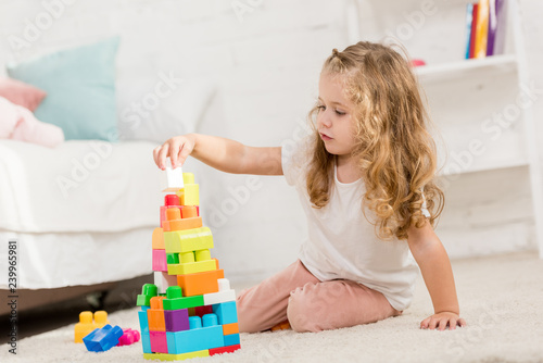 adorable kid playing with colored plastic constructor on carpet in children room