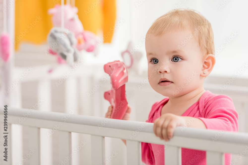 adorable child in pink shirt holding pink joystick in crib adorable child in pink shirt holding pink joystick in crib