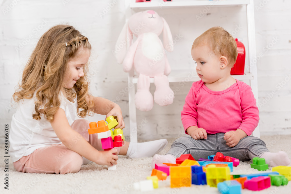adorable sisters playing with constructor together on carpet in children room adorable sisters playing with constructor together on carpet in children room
