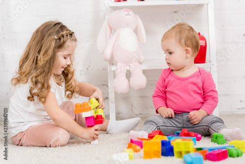 adorable sisters playing with constructor together on carpet in children room